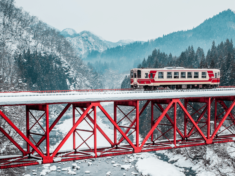 The Akita Nairiku Line passes over a red bridge during the winter