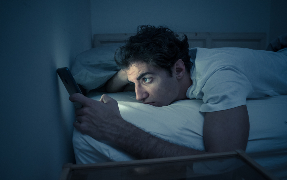 man lying in bed looking as his phone