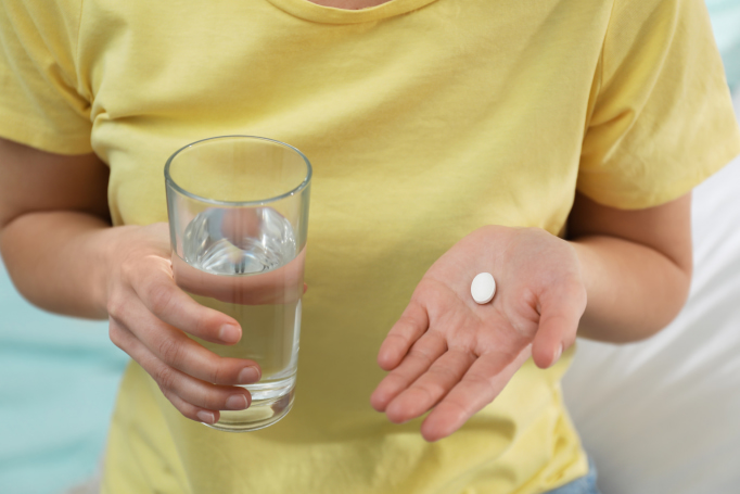 person holding pill and glass of water
